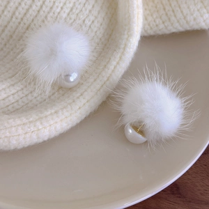 Detailed close-up of winter white fluffy pom pom earrings with elegant pearl accents