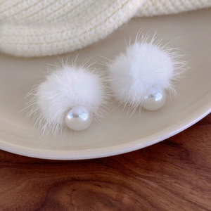 Close-up of white fluffy pom-poms and pearl earrings on a warm aesthetic background