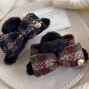 Close-up of plaid fabric bow hair claws with pom-poms and golden metal charms on ceramic