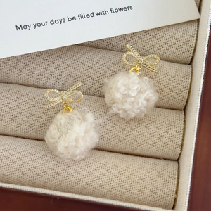 Detail of gold bow earrings with pavé zircons and white plush faux fur pom pom