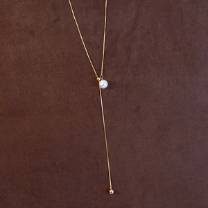 Macro detail of a gold Y-shaped adjustable pearl necklace on a dark brown suede surface