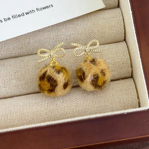 Detail of plush leopard print faux fur ball earrings with sparkling bow studs in a gift box