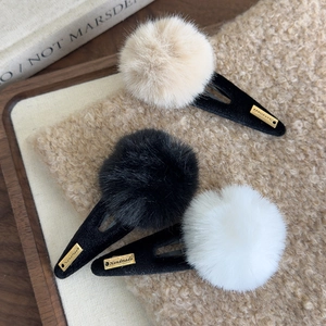 Détail de trois barrettes à pompons en peluche beige noir et blanc sur plateau en bois