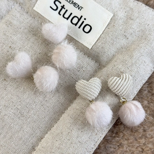 Detailed view of winter plush heart earrings and fuzzy pompom studs in beige