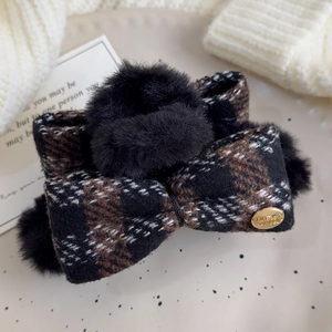 Detail of tweed bow hair claw with black faux fur poms and engraved gold metal tag