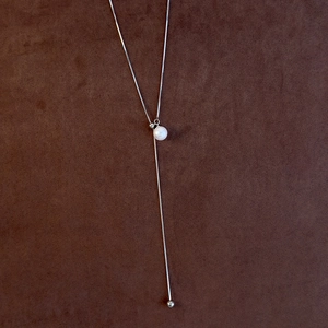 Detail of adjustable silver Y-shaped necklace with pearl pendant on brown background