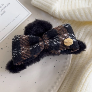 Close-up of checkered plush hair claw clip featuring a gold metal engraved tag