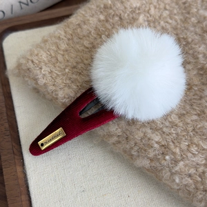 Macro d'une pince à cheveux en velours bordeaux avec pompon blanc et badge artisanal