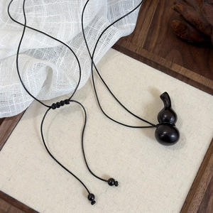Détail d'un pendentif gourde en bois noir sur un cordon noir avec un décor artistique