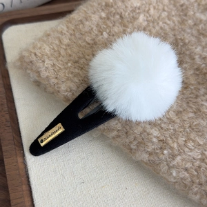 Détail d'une pince à cheveux avec pompon blanc et plaque dorée sur velours noir