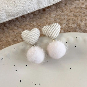 Detail of heart-shaped corduroy and soft pink faux fur pompom earrings on a white plate