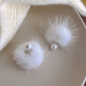 Detailed view of white faux mink fur earrings with elegant pearl center on ceramic tray