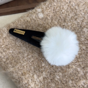 Détail d'une pince à cheveux en peluche blanche avec étiquette dorée Handmade sur tissu