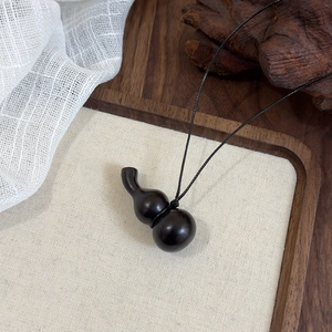 Vue rapprochée du pendentif gourde en ébène poli avec cordon en cuir noir sur lin