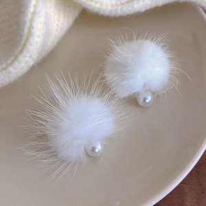 Close-up of white plush pompom and pearl earrings on a ceramic dish with knit fabric