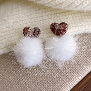 Close-up of brown plaid heart and fluffy white faux fur pom poms on beige knit fabric