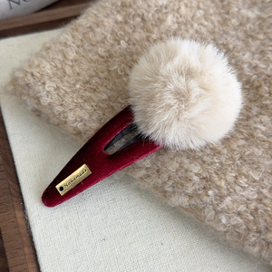 Détail d'une pince à cheveux en velours rouge avec pompon en peluche et logo fait main