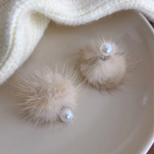 Detail of beige faux fur pom pom earrings with pearl accents on a ceramic tray
