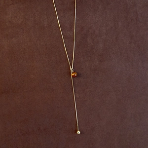 Detail of adjustable gold Y-necklace with tiger eye stone bead on brown velvet background