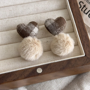 Detail view of coffee plaid heart earrings with beige faux fur pompoms in a wooden box