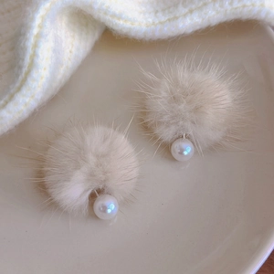 Close-up of elegant cream faux fur ball earrings with shimmering pearl accents on knit fabric