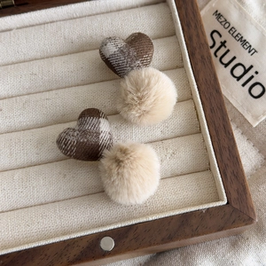 Close-up of brown plaid heart and plush pom-pom earrings in a wooden jewelry box