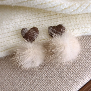 Close-up of heart-shaped brown plaid fabric earring with a soft cream plush pom pom