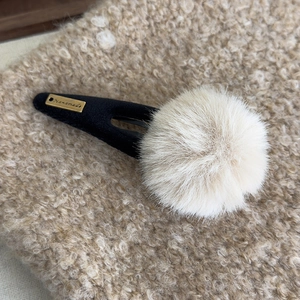 Détail de la pince à cheveux avec pompon en peluche et étiquette dorée faite main
