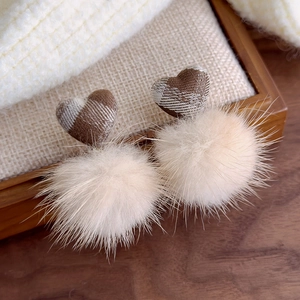 Macro view of brown plaid heart and soft plush ball charm on stylish winter earrings