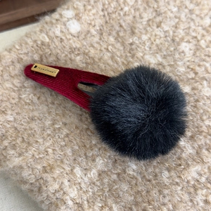 Détail d'une pince en velours rouge avec pompon noir et étiquette dorée