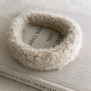 Detailed texture of beige boucle wool headband placed on a minimalist book cover