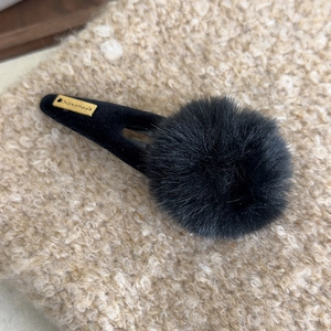 Détail d'une pince à cheveux noire en peluche avec pompon et plaque dorée faite à la main