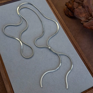 Macro shot of silver snake chain necklace coiled on grey felt tray with wooden accents