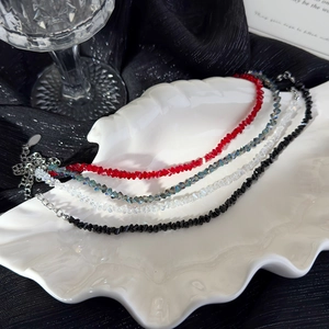 Handmade beaded crystal bracelets in red, black, and iridescent tones on a white shell plate