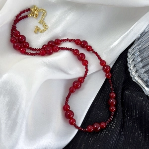 Vintage burgundy beaded necklace with gold lobster clasp on elegant fabric background