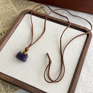 Dettaglio del ciondolo in cristallo viola a forma di borsa con finiture in metallo oro
