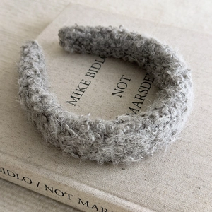 Close-up of a grey plush lamb wool headband with curly texture on a vintage book