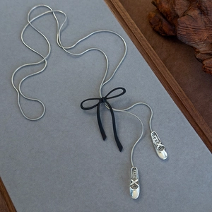 Detail of silver snake chain with matte black bow and ballet slipper pendants on felt