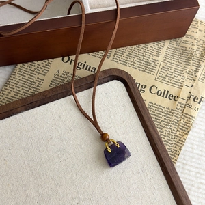 Dettaglio macro del ciondolo a borsa in pietra viola su cordino marrone e perla in legno
