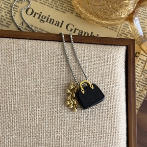 Detail of necklace pendant with black handbag design and golden bead cluster on silver chain