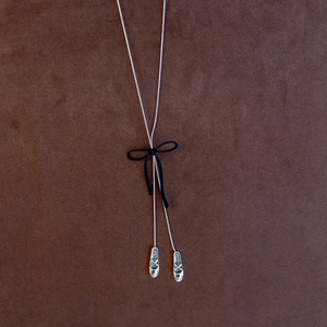 Detailed macro view of silver Y-necklace with blue bow and ballet shoes pendants
