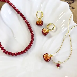 Elegant pomegranate red bead necklace with gold pendant jewelry set on a white shell tray