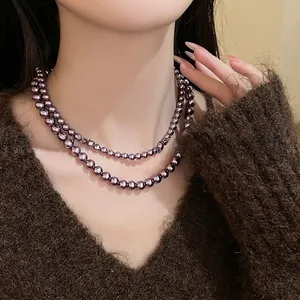 Dettaglio collana a due fili di perle di vetro viola scuro su un maglione di maglia