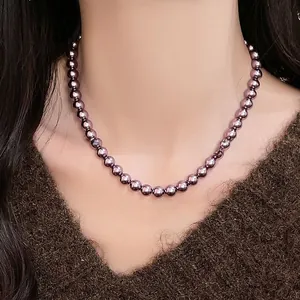 Vista dettagliata della collana di perle viola scuro su un maglione marrone