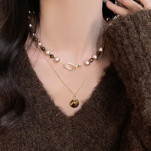 Détail d'un collier à deux rangs orné de pierres œil de tigre et perles sur un pull marron