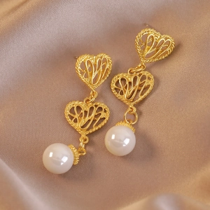 Orecchini a cuore vintage dorati con perle bianche su sfondo in seta di lusso