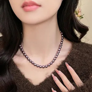 Elegante collana di perle di vetro viola scuro indossata su un maglione di maglia marrone