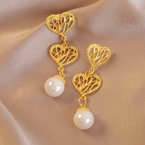 Orecchini pendenti vintage a cuore dorato con perle bianche su sfondo di seta