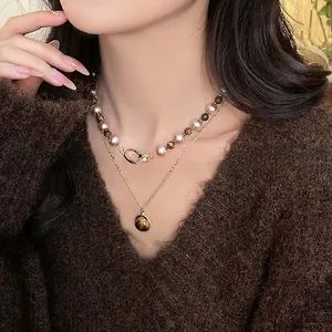 Détail de colliers superposés en œil de tigre et perles sur un mannequin en pull marron