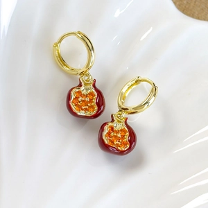 Detailed close-up of gold-plated red pomegranate drop earrings on a white shell tray